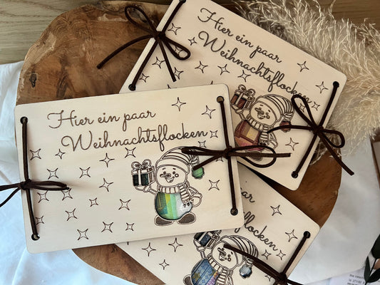 Geldgeschenk für Weihnachten. Mit dem Spruch: Hier ein paar Weihnachtsflocken. Der Schneemann ist ausgeschnitten, wodurch das Geld zum vorschein zwischen die 2 Holzkarten kommt.