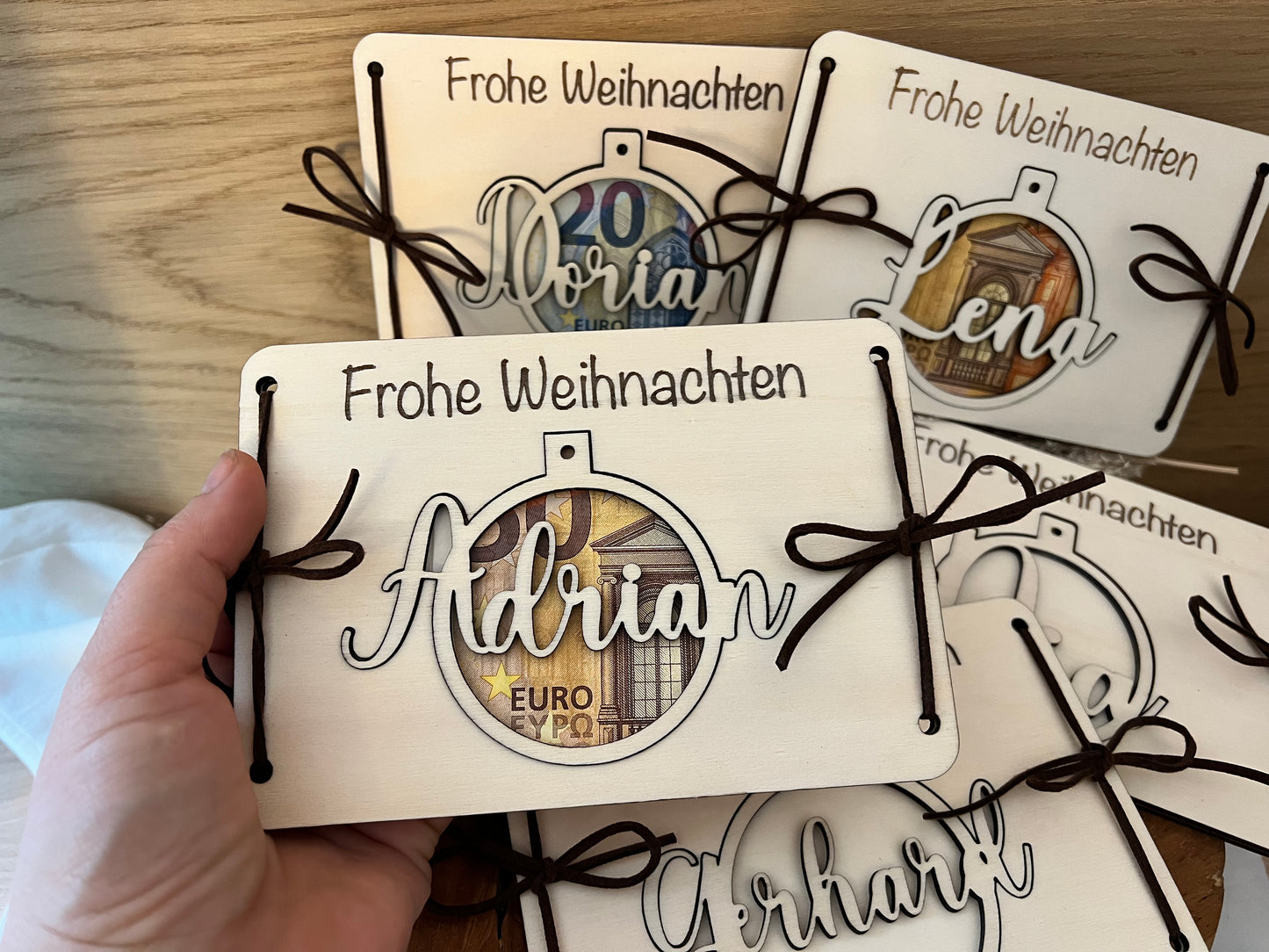 Personalisiertes Geldgeschenk in einer Weihnachtskugel. Das Geld wird zwischen den 2 Holzkarten eingelegt. Die Weihnachtskugel wird mit deinem Wunschnamen personalisiert. Damit kann man auch den Weihnachtsbaum schmücken.